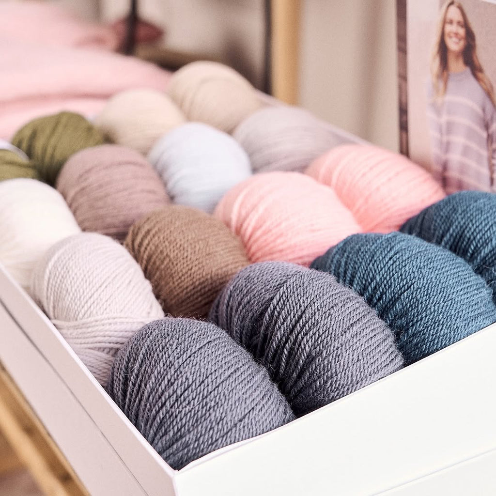 A collection of vibrant Alpaca-wool-Mode-Rowan yarns is displayed in a room featuring a framed picture of a woman nearby.