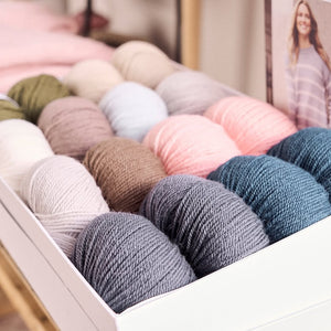 A collection of vibrant Alpaca-wool-Mode-Rowan yarns is displayed in a room featuring a framed picture of a woman nearby.