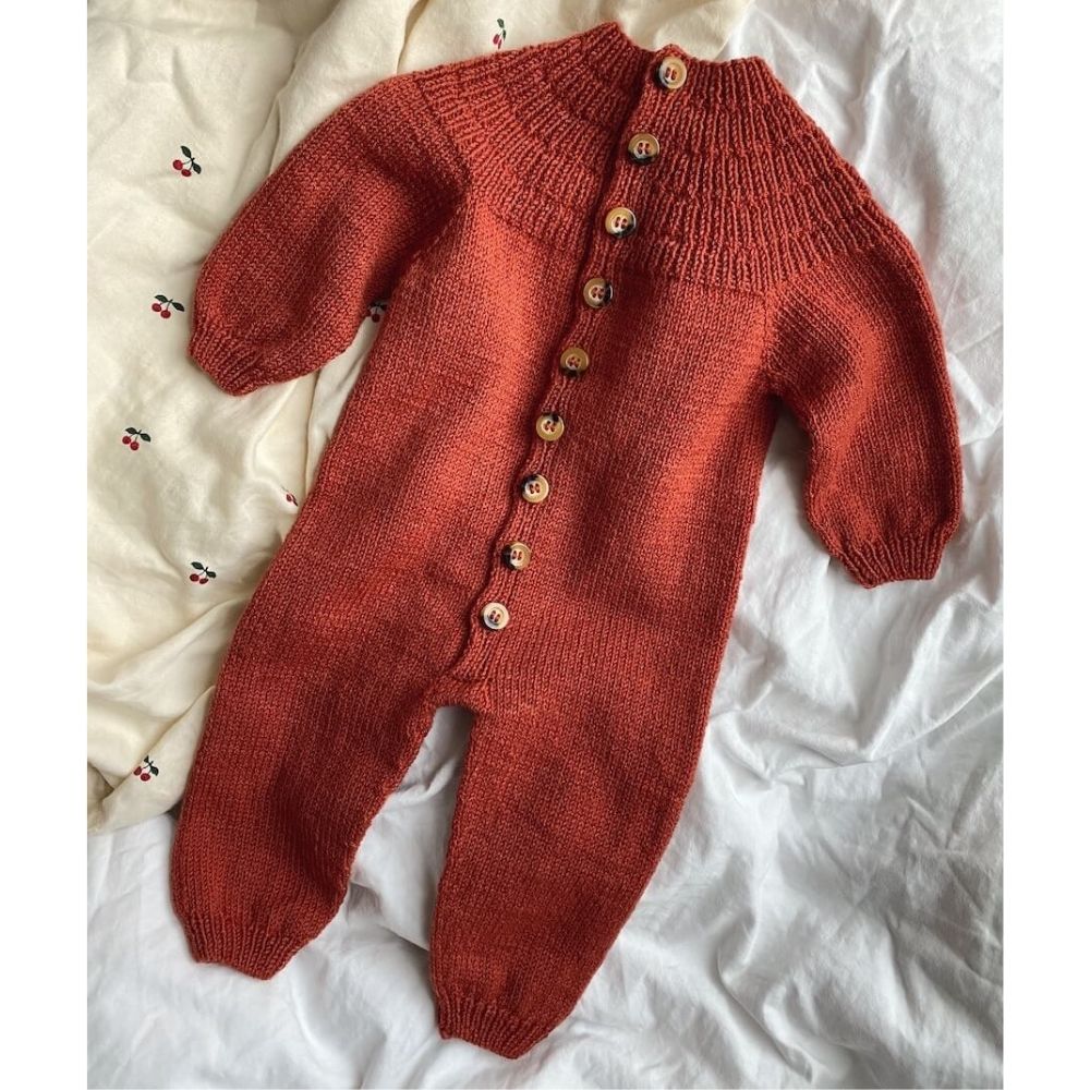 A knitted red baby onesie featuring buttons, designed with a circular yoke and ribbed plackets for easy dressing.