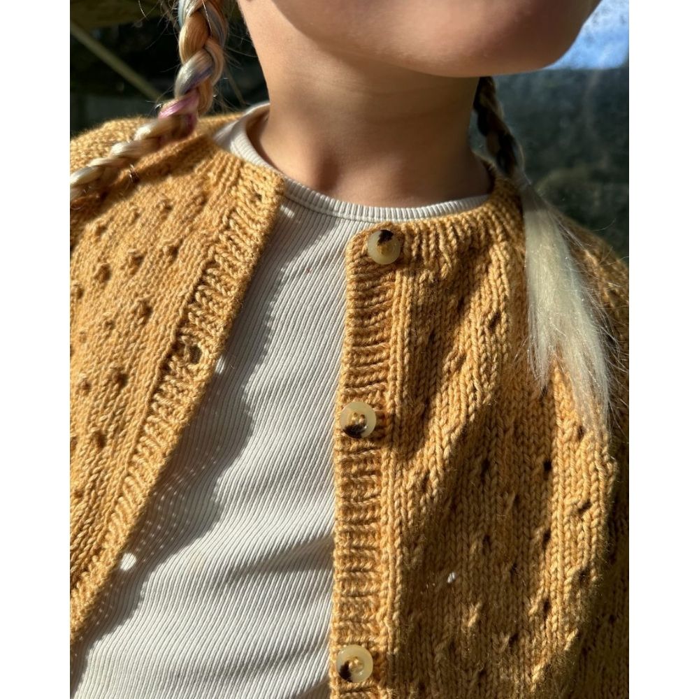 A young girl dressed in a yellow cardigan, highlighting a lovely lace pattern and neatly finished button edges.