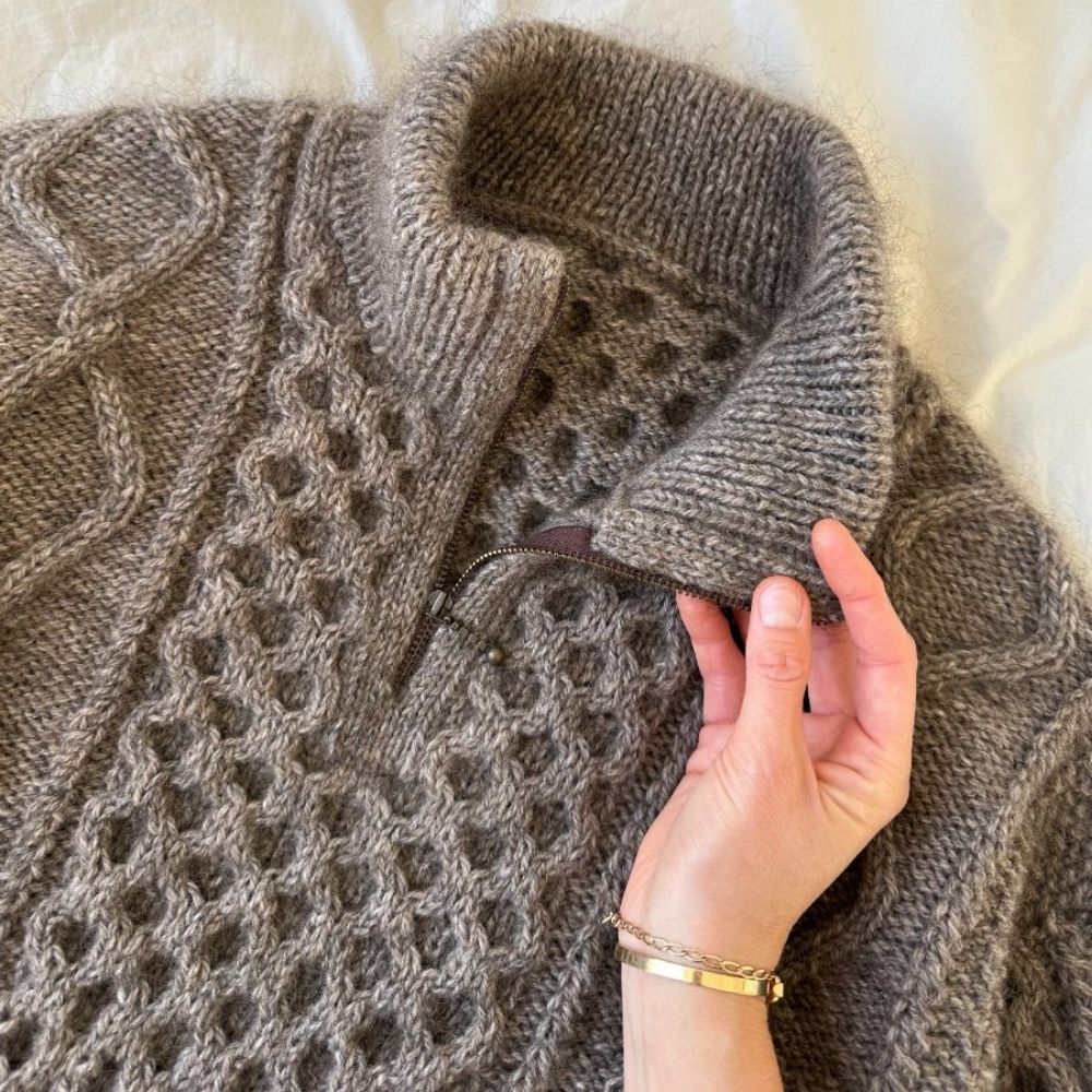 A woman holds a zipped sweater, showcasing intricate cable and texture patterns, designed for a stylish, cozy fit.