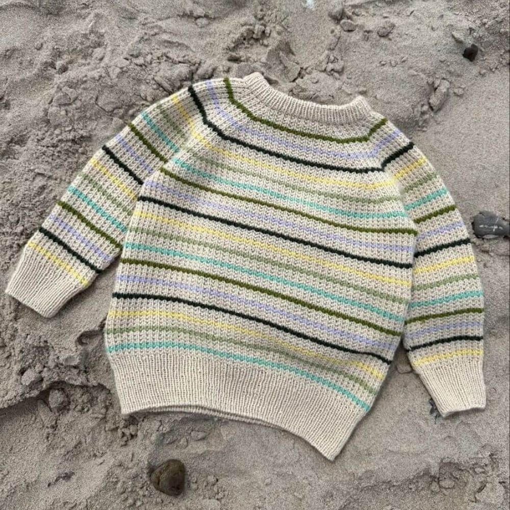 friday sweater  lies on the sandy beach, featuring ribbed cuffs and hem, perfect for a relaxed coastal day.