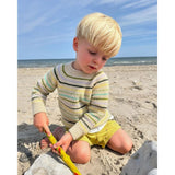 A young boy  wearing friday sweater engaged in building sandcastles on the beach, surrounded by a bright and sunny atmosphere.