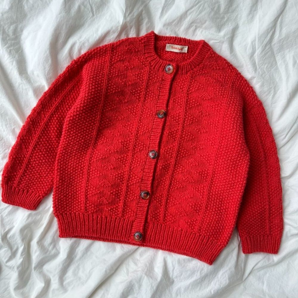 A red cardigan sweater neatly laid on a bed, showcasing its textured pattern and elegant design.