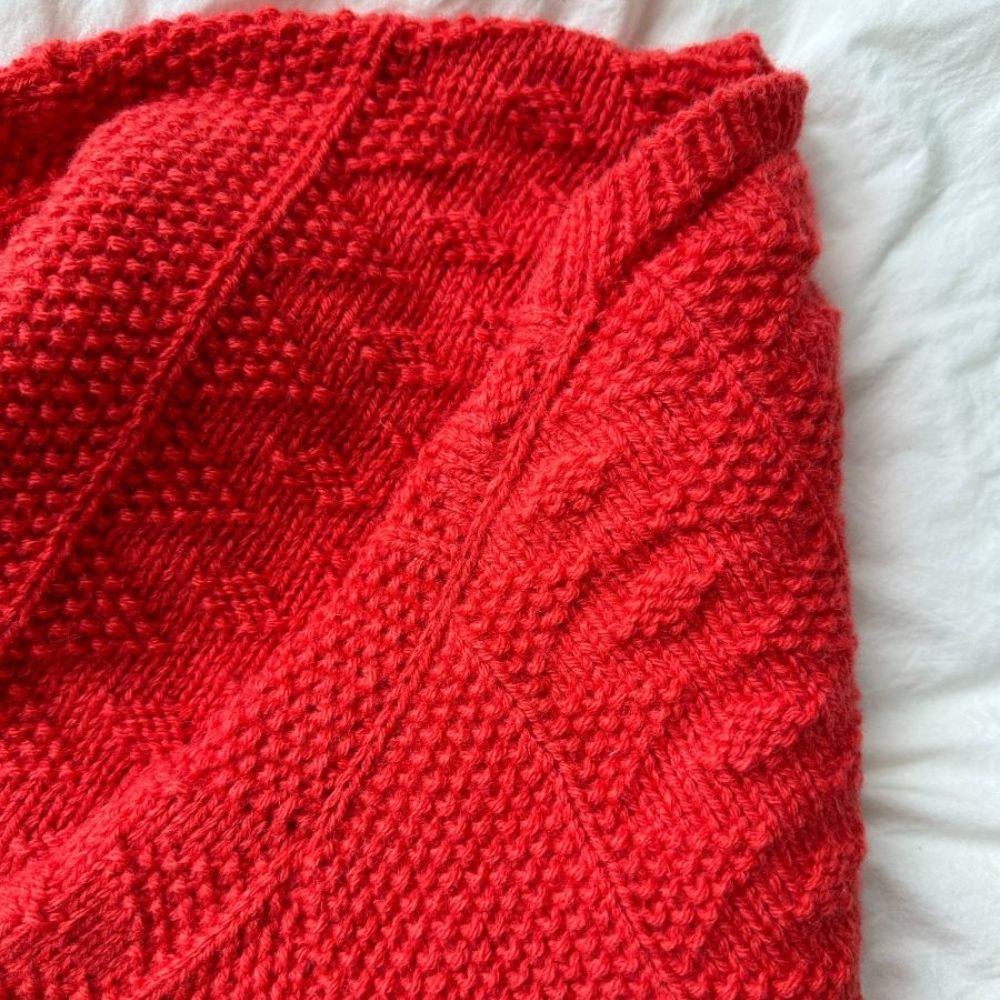 A cosy red knitted blanket draped elegantly over a bed, adding warmth and color to the room's decor.