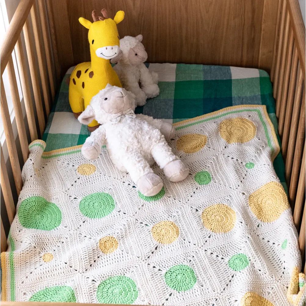 Crocheted blanket with circular patterns in a crib with stuffed animals