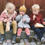 Three children sitting on steps, enjoying lollies on a sunny day, with smiles on their faces.