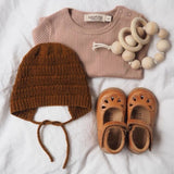 A baby's outfit, including the anker bonnet with tie-strings, neatly arranged on a soft bedspread.