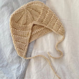 A knitted anker bonnet hat resting on a bed, showcasing its ribbed segments and i-cord edge with tie-strings.