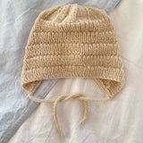 A knitted anker bonnet hat resting on a bed, showcasing its ribbed segments and i-cord edge with tie-strings.