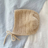 A knitted bonnet displayed on a bed, highlighting its ribbed design and finished with an i-cord edge and ties.
