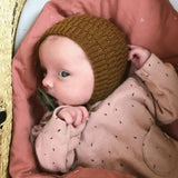  A baby wearing a knitted hat and a pink shirt, featuring a delightful design with tie-strings for a secure fit.