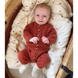 An infant dressed in a vibrant red anker onesie is nestled in a basket, exuding warmth and charm.