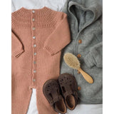 A baby's sweater, shoes, and brush neatly arranged on a bed, showcasing adorable infant clothing and accessories.