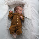 A baby in a brown sweater peacefully resting on a bed, showcasing the cozy design of Anker’s Onesie.