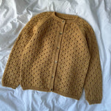 A yellow cardigan sweater draped elegantly on a bed, showcasing its delicate lace pattern and top-down construction.