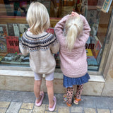 Two small girls look intently at books in a window, showcasing their interest in reading and exploration, wearing their warm sweaters.