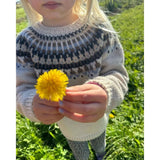 A little girl joyfully holds a dandelion, while wearing the celeste sweater.