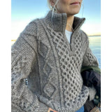 A woman in a cable-knit sweater highlights the unique texture and design, featuring a zipper along the front opening.