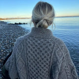 A woman wearing a cozy sweater stands on the beach, highlighting the detailed design of the Dagmar Zipper Sweater.