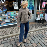 A woman in the dagmar sweater and jeans stands on a cobblestone street, highlighting a fashionable yet comfortable appearance.