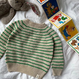 A charming baby  friday sweater adorned with blocks and toys, resting on a bed, emphasizing its cozy and inviting appearance.