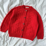 A red cardigan sweater neatly laid on a bed, showcasing its textured pattern and elegant design.
