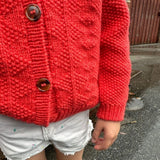 A young girl wearing a red sweater and shorts, radiating joy and energy in a casual outdoor environment.