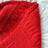 A cosy red knitted blanket draped elegantly over a bed, adding warmth and color to the room's decor.