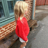 A young girl wearing a vibrant red sweater and white sneakers, enjoying a sunny day in the park