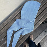 Light blue knit hooded scarf laid on a wooden bench, with a pair of shoes visible nearby, on pavement.