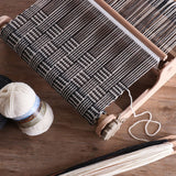 A compact weaving loom, yarn, and needles arranged on a wooden table, ideal for both new and experienced weavers.