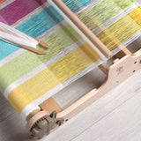 A multi-colored woven cloth displayed on a wooden table, showcasing the vibrant patterns created by a compact weaving loom.